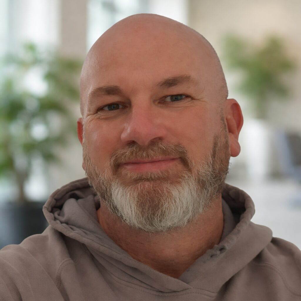 David smiles at the camera, he has a beard and is wearing a brown hoodie.