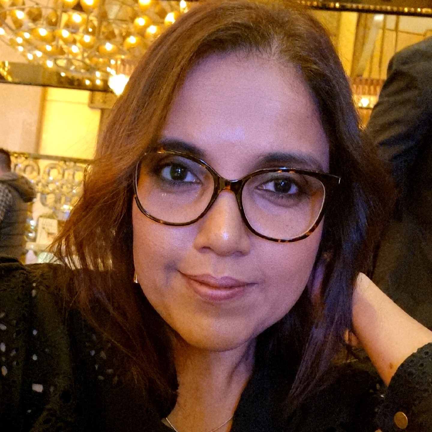 Dinishi smiles, she has long dark hair and is wearing dark framed glasses.