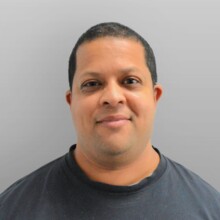 Dom wears a black t-shire and it looking at the camera