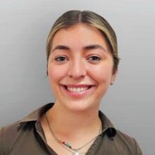 Mia is smiling at the camera and is wearing a brown top and a colourful necklace