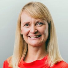Natalie is wearing a bright red top and has long blonde hair, smiles widely at the camera