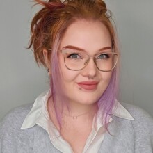 Morgan smiles for the camera. She is wearing glasses and has auburn and purple hair.