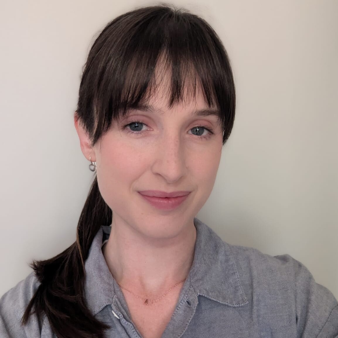 Anna has shoulder length brown hair sitting on her and is wearing a grey shirt