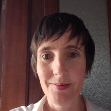 Elissa has short brown hair and is wearing a white shirt