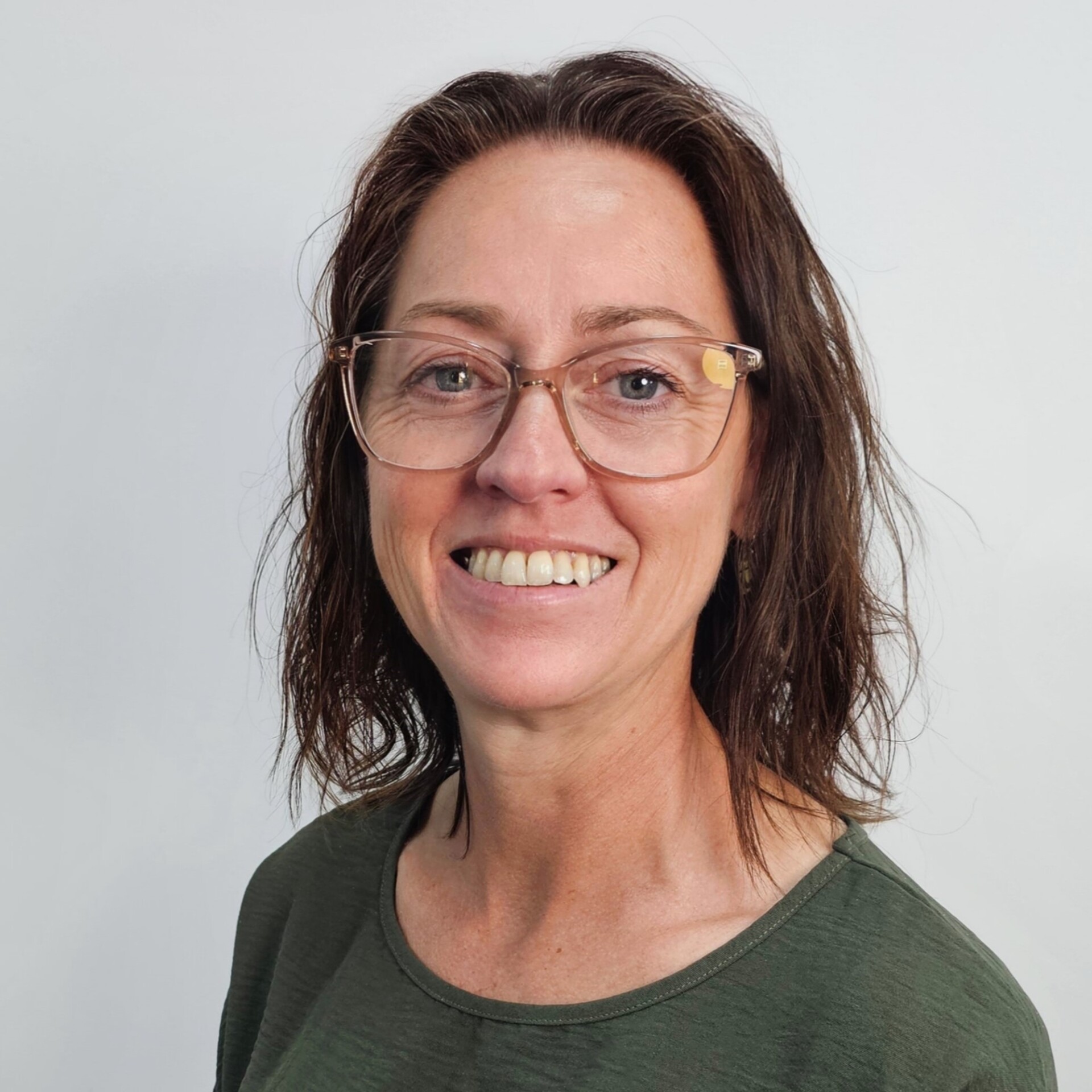 Jane has mid to dark, shoulder-length hair. She is wearing glasses and she is smiling.