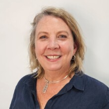 Michelle smiles for the photo in front of a plain white background. She has short light hair and is wearing a dark blue blouse.