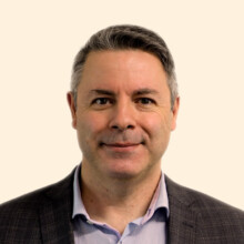 Headshot of Philip, he wears a blue shirt under a black jacket, he has short dark hair and smiles slightly at the camera