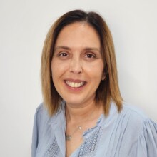 Sally smiles for her photo. She has should length dark hair with highlights and is wearing a light top.