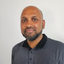 Utpal smiles to the camera. He has short facial hair and is wearing a dark polo shirt.