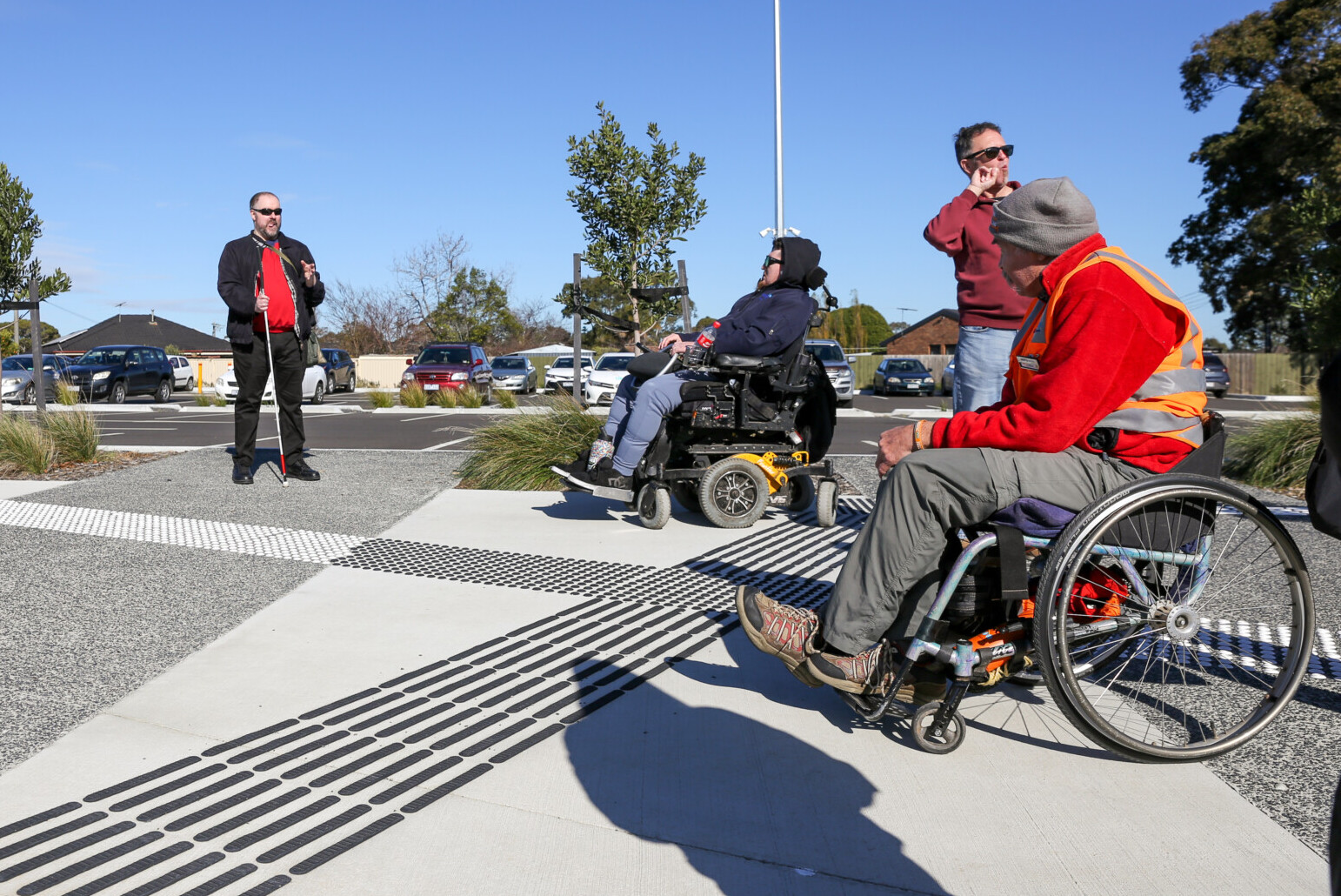 A group of people, including wheelchair users and a white cane user, gather in an outdoor area being assessed for accessibility with our Inclusive Design team.