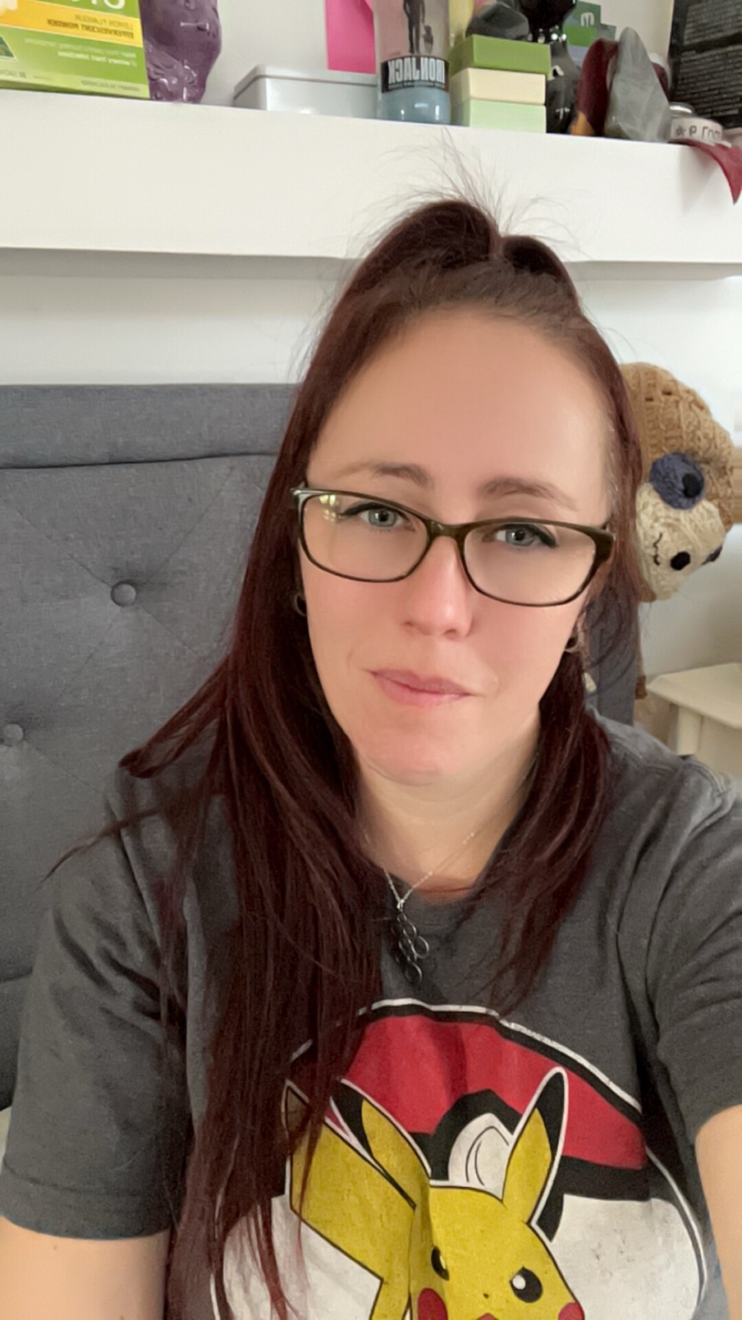 Claire has shoulder length brown hair is wearing glasses and a grey shirt with a pic on the front