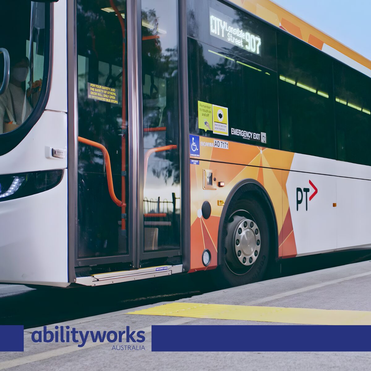 A victorian public transport bus with orange and white livery is parked at a bus stop on a sunny day.There is a yellow tactile paving strip on the ground beside the bus.