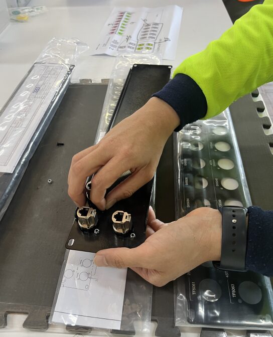 An employee assembles small silver pieces in a black panel.