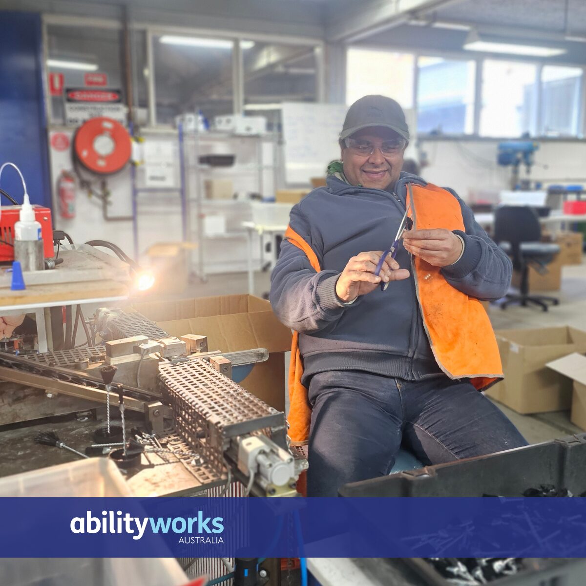 An employee smiles at his workstation. He is using scissors to cut stray hairs from a freshly made brush.